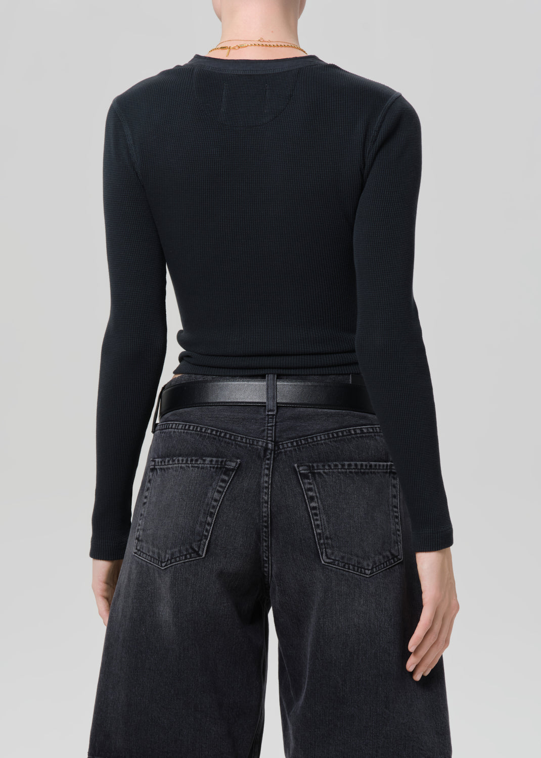 Person wearing a black long-sleeve top and black denim shorts on a plain background