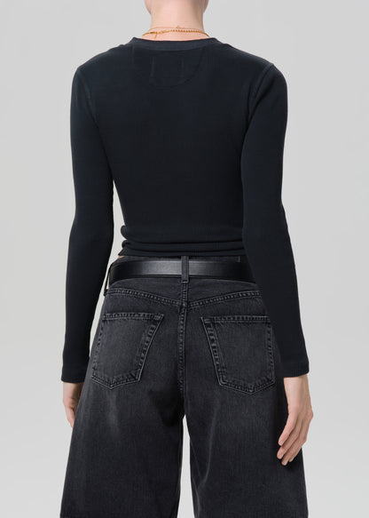 Person wearing a black long-sleeve top and black denim shorts on a plain background