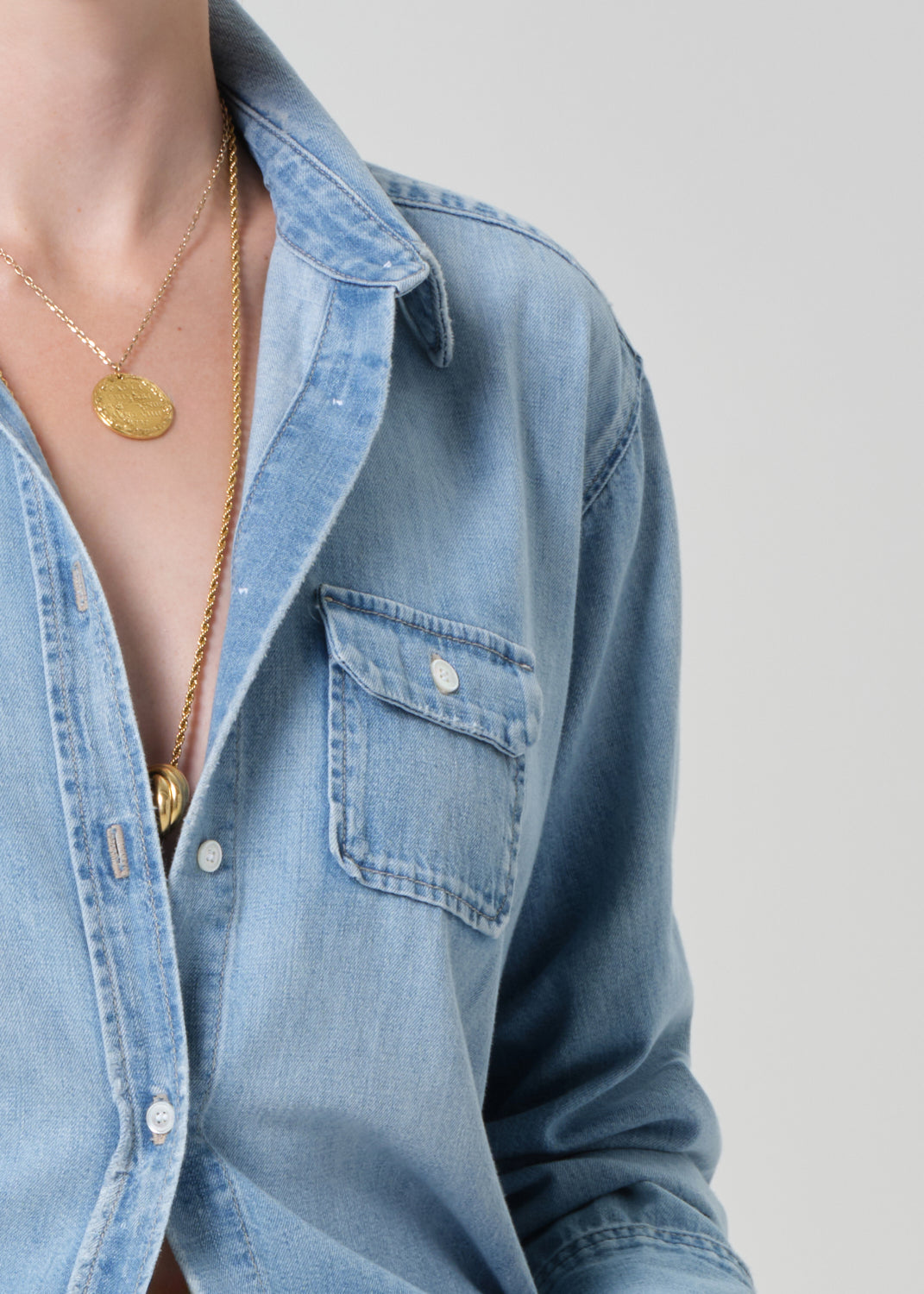 Close-up of a person wearing a blue denim shirt with a gold necklace on a plain background