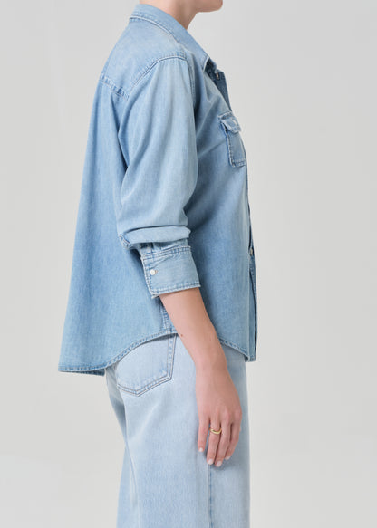 Person wearing a light blue denim shirt and jeans on a plain background