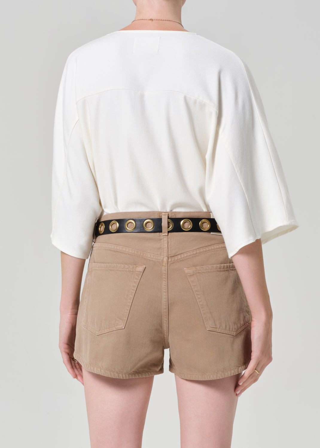 Person wearing a white blouse and beige shorts with a decorative belt on a plain background