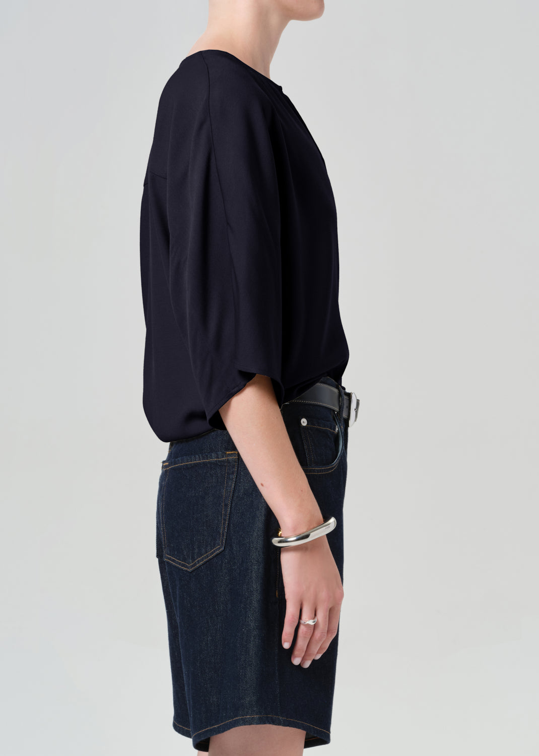 Person wearing a navy blouse with a deep neckline and dark denim shorts on a light gray background