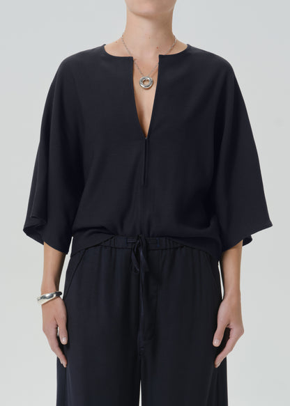 A model wearing a black wide-sleeve top with a split neckline and matching black drawstring trousers, styled with a silver pendant necklace and bracelet against a grey
background.
