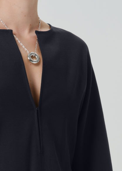Close-up of a person wearing a silver-toned double-ring pendant necklace over a black top, against a grey background.