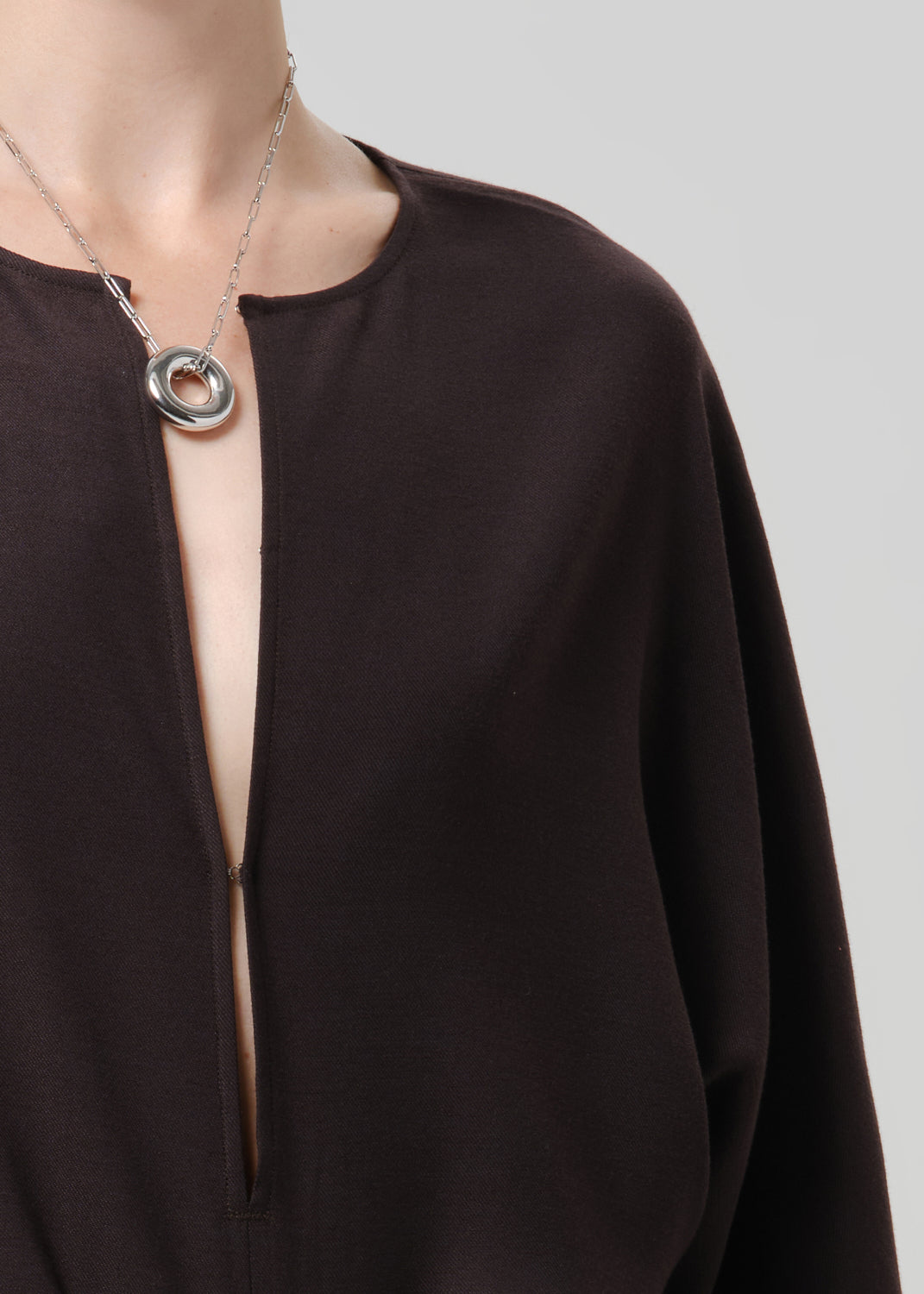 Close up of brown shirt and silver jewelry on a grey background