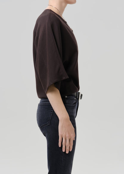 Person wearing brown top with black belt and dark blue pants on a grey background