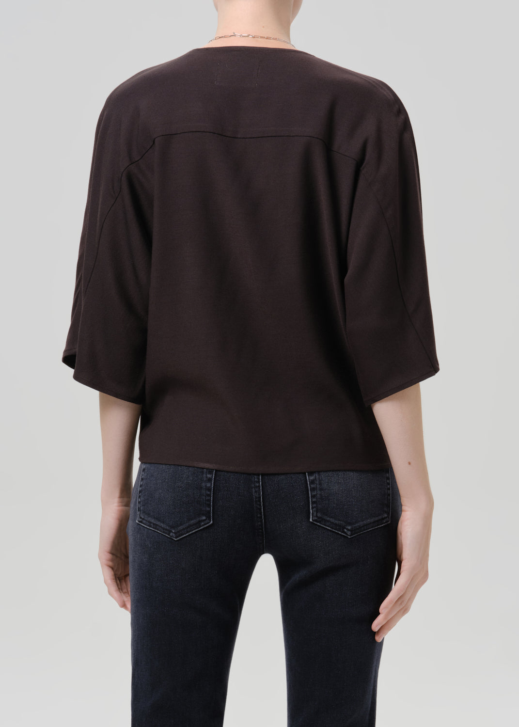 Person wearing brown top with black belt and dark blue pants on a grey background
