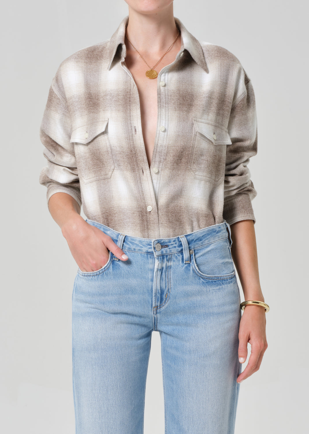 Person wearing a patterned shirt and light blue jeans on a plain background