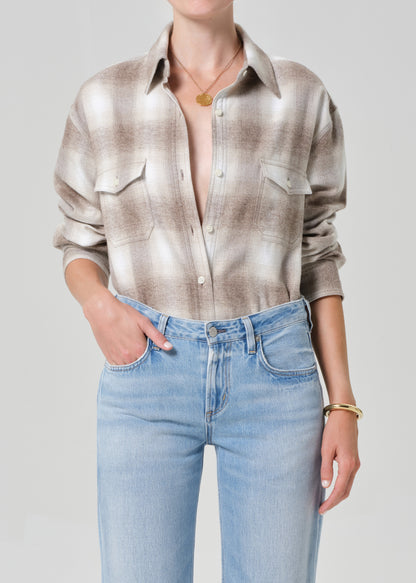 Person wearing a patterned shirt and light blue jeans on a plain background