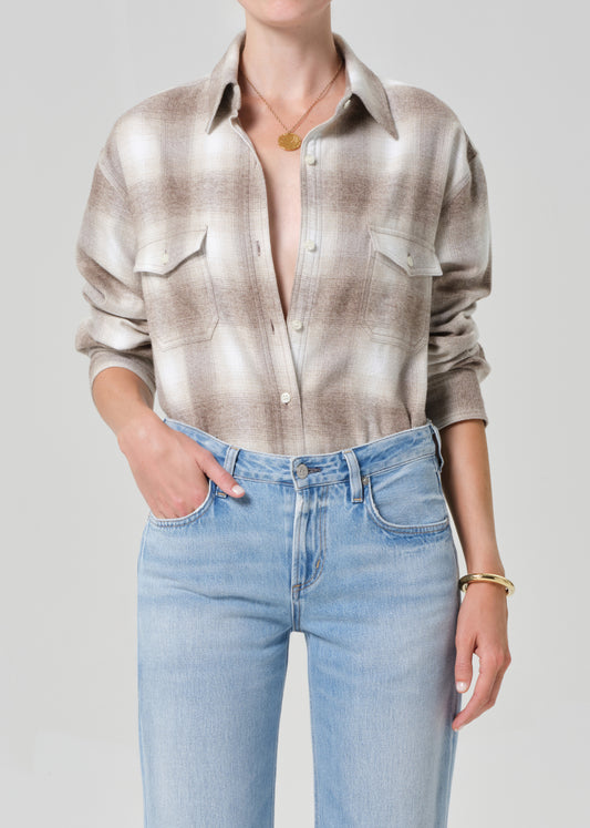 Person wearing a patterned shirt and light blue jeans on a plain background