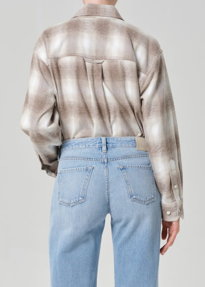 Person wearing a patterned shirt and light blue jeans on a plain background