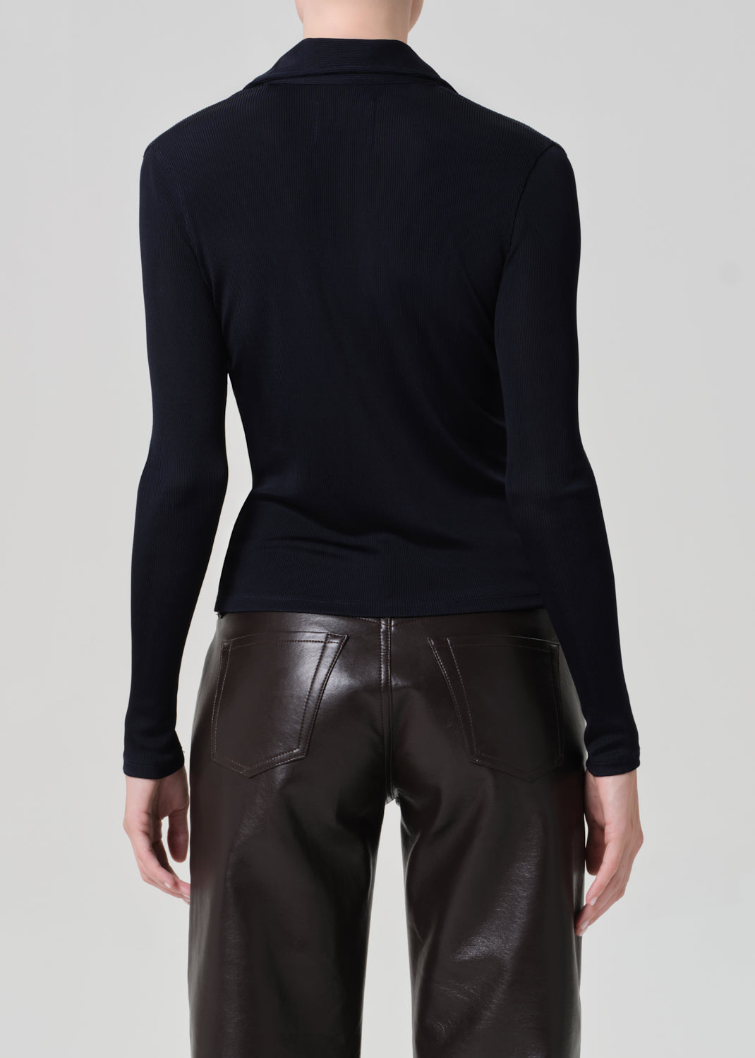 Person wearing a navy shirt and leather brown pants on a plain background