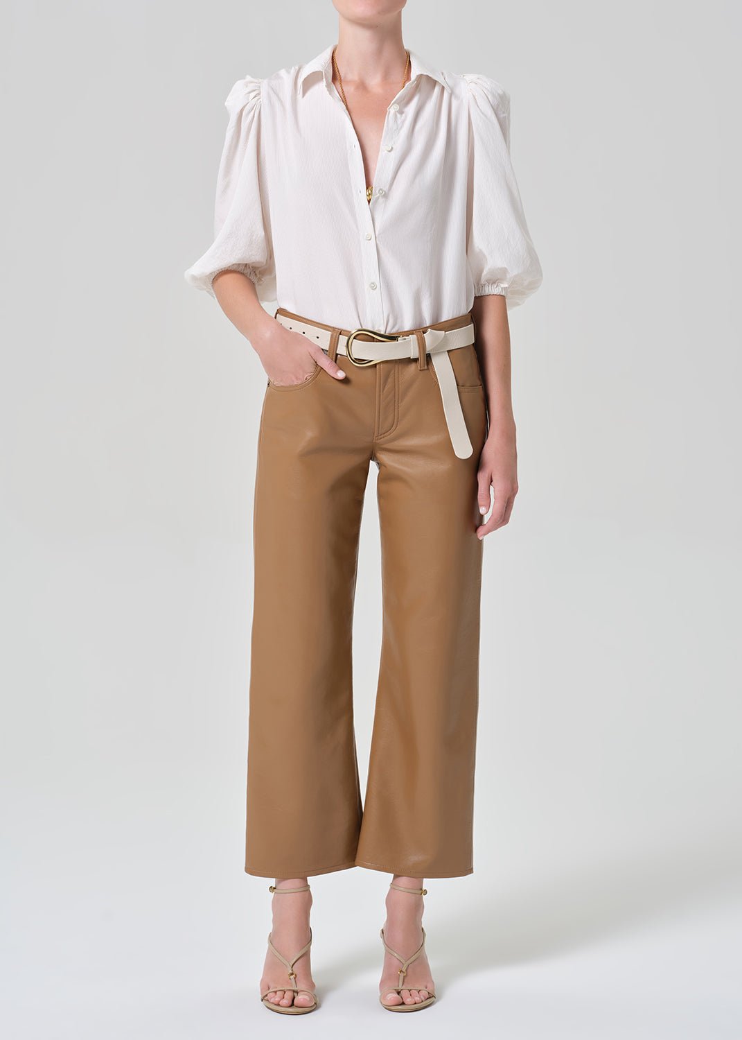 Person wearing a white blouse with puff sleeves and brown leather pants on a plain background
