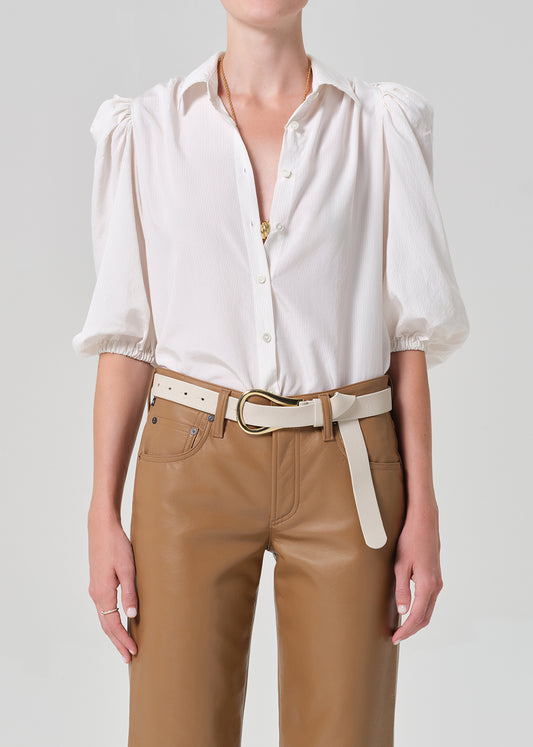 Person wearing a white blouse with puff sleeves and brown leather pants on a plain background