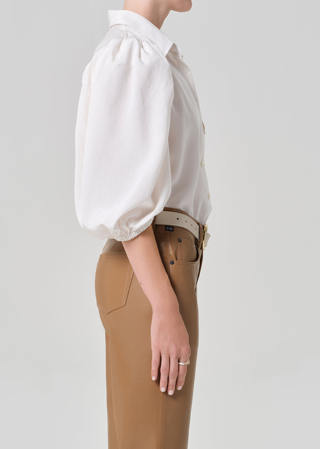 Person wearing a white blouse with puff sleeves and brown leather pants on a plain background