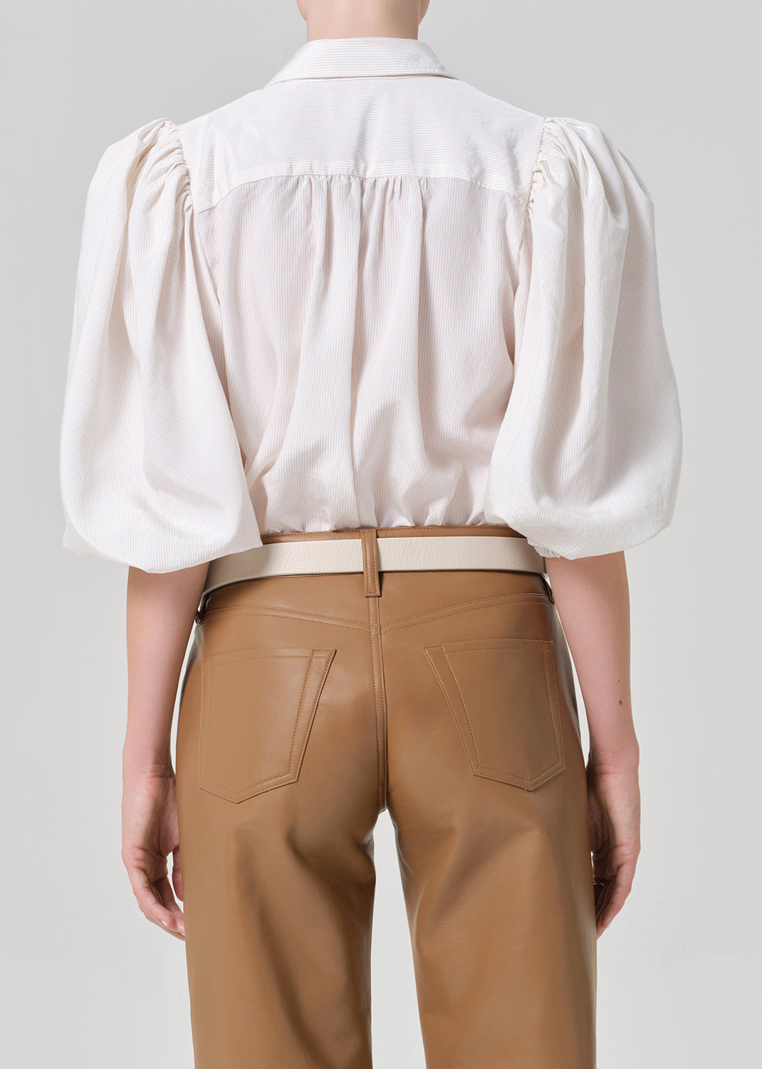 Person wearing a white blouse with puff sleeves and brown leather pants on a plain background