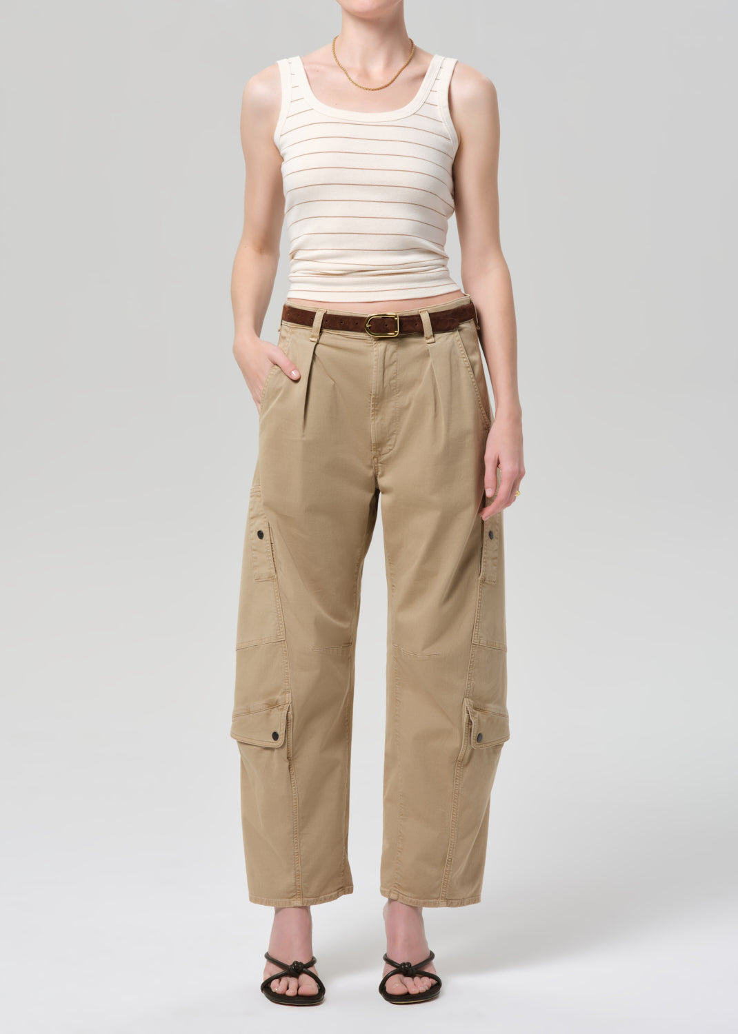 Person wearing a beige tank top and cargo pants on a grey background