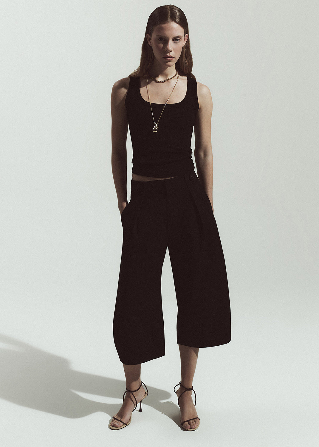 Woman wearing a black sleeveless top and wide-leg pants on a white background