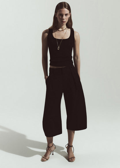 Woman wearing a black sleeveless top and wide-leg pants on a white background