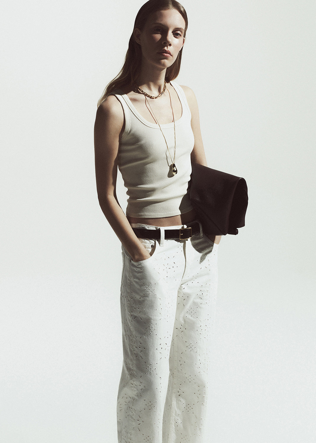 Woman wearing a white tank top and white pants against a plain background