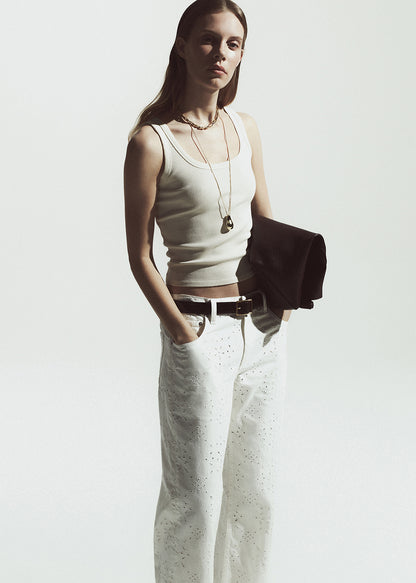 Woman wearing a white tank top and white pants against a plain background