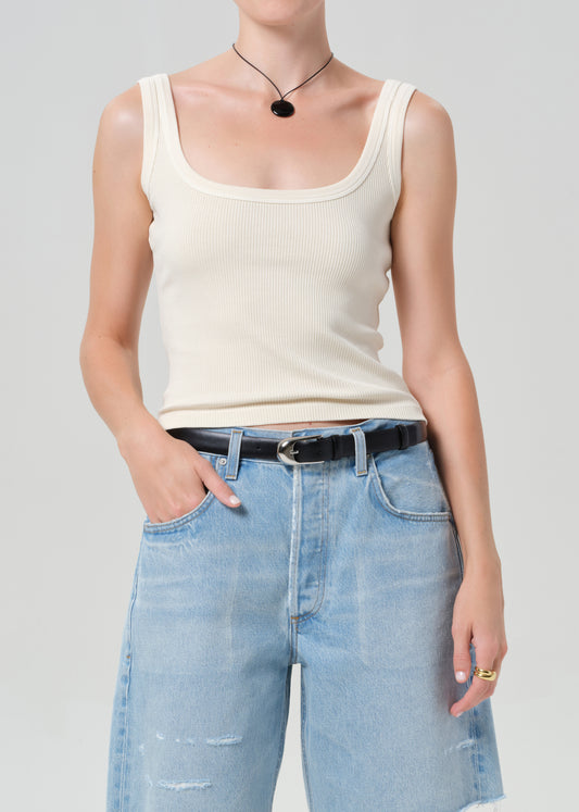 Person wearing a beige tank top and blue jeans on a plain background