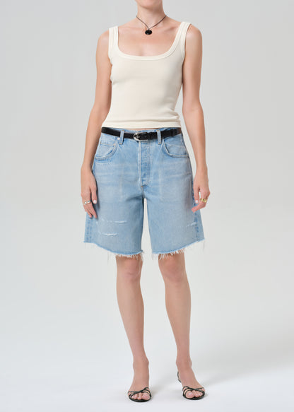 Person wearing a white tank top and light blue denim shorts on a plain background