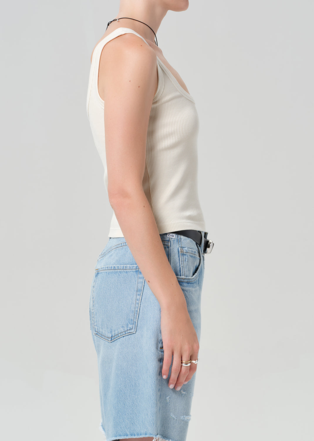 Person wearing a white sleeveless top and light blue denim shorts on a plain background