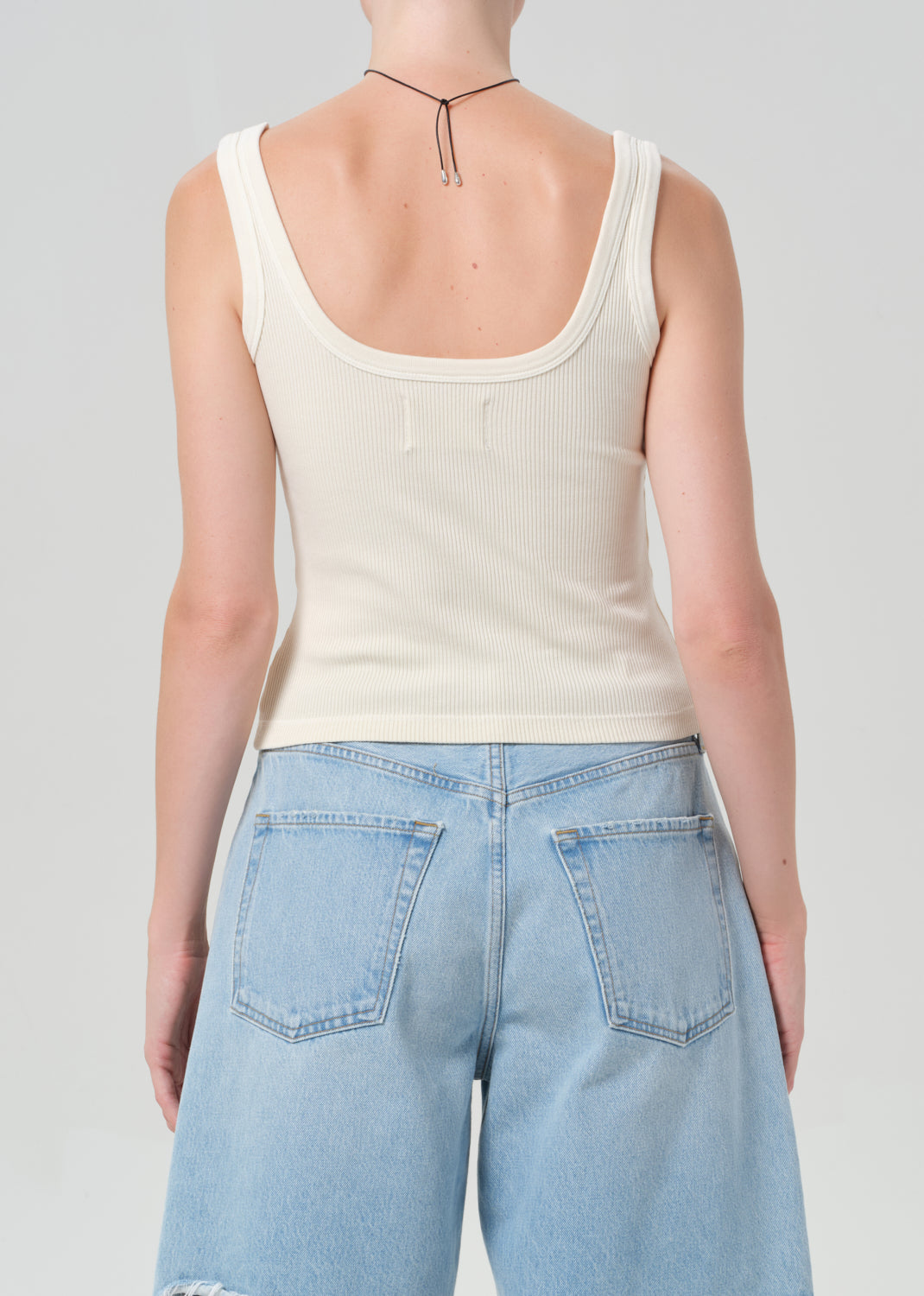 Person wearing a beige tank top and light blue jeans on a plain background