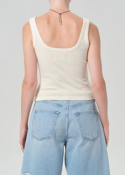 Person wearing a beige tank top and light blue jeans on a plain background