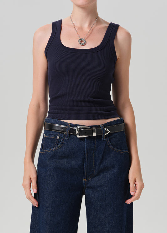 A model wearing a dark navy ribbed tank top tucked into dark blue jeans with a black belt, shot against a grey background.