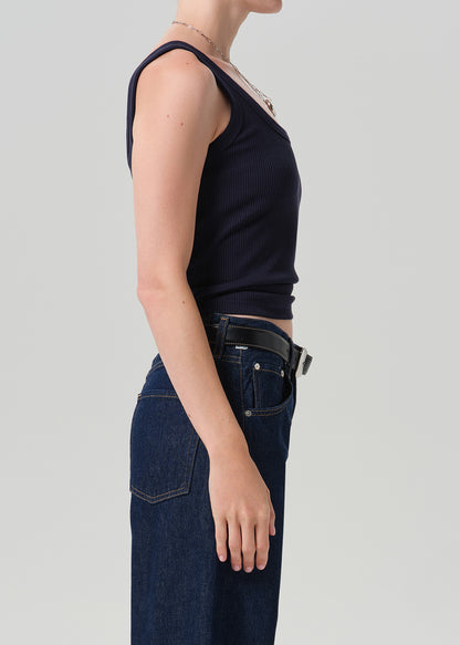 A side-profile view of a model wearing a dark navy ribbed tank top and dark blue jeans with a black belt, against a grey background.