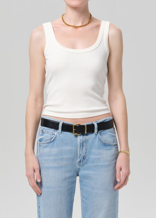 Person wearing a white tank top and light blue jeans with a black belt on a gray background