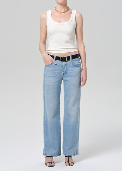 Person wearing a white tank top and light blue jeans on a plain background
