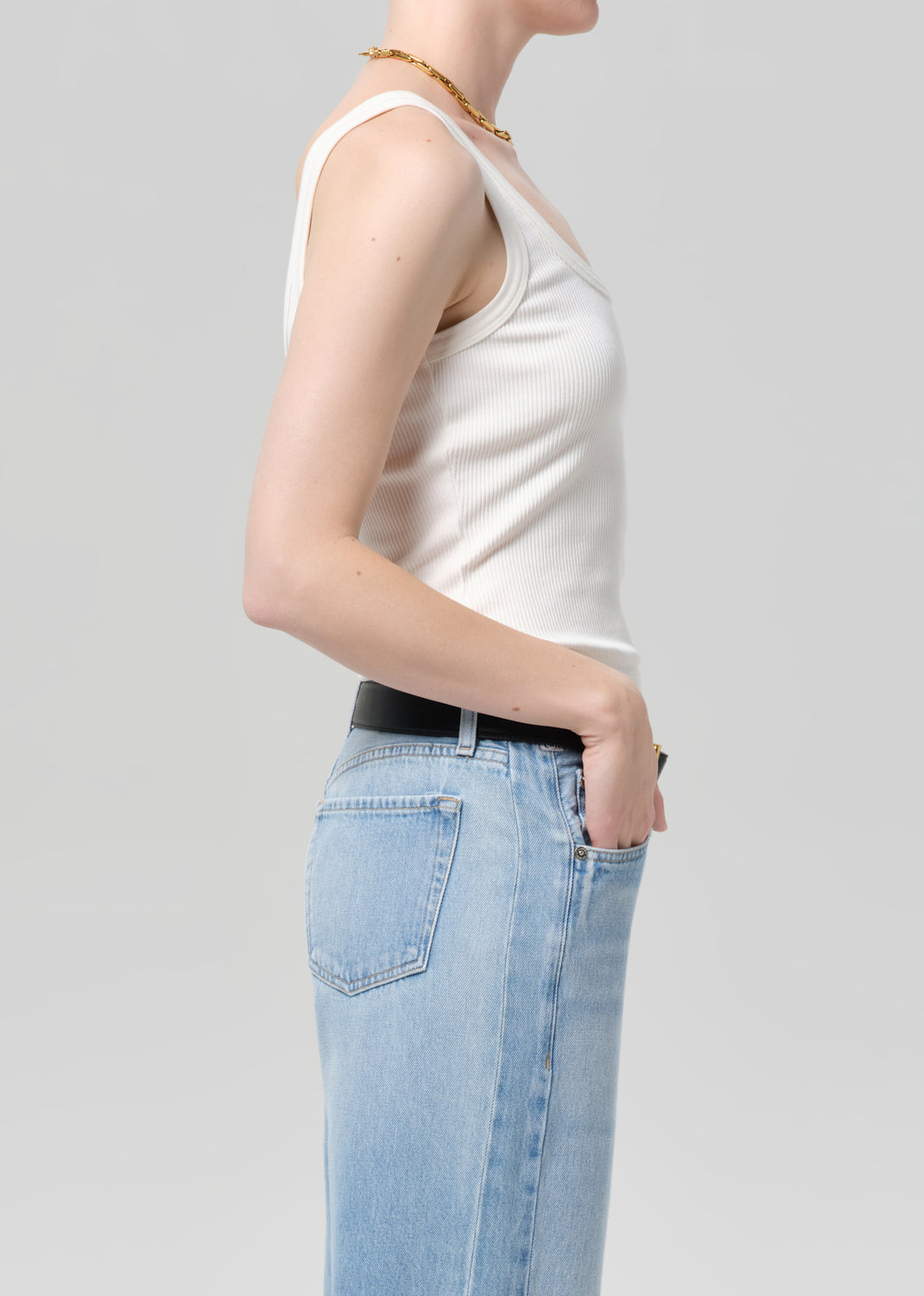 Person wearing a white tank top and light blue jeans on a plain background