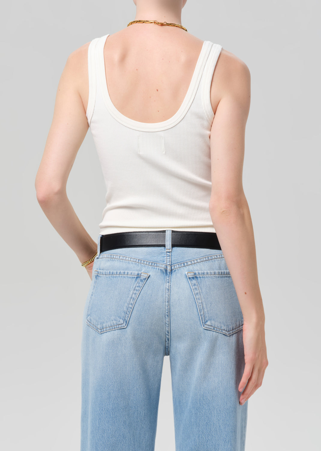 Person wearing a white tank top and light blue jeans on a plain background