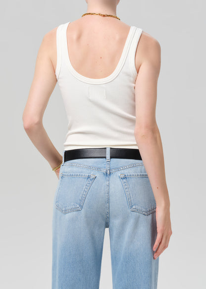Person wearing a white tank top and light blue jeans on a plain background
