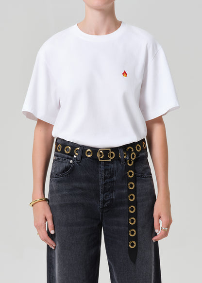 Person wearing a white t-shirt with a red logo and dark jeans on a plain background