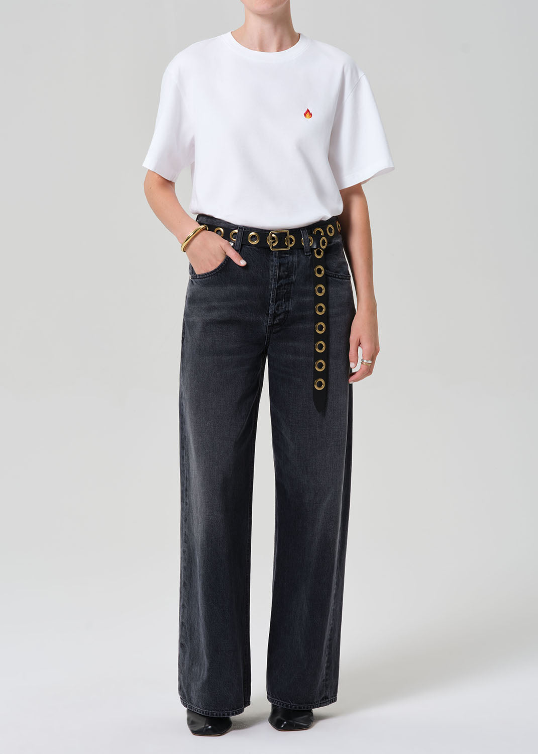 Person wearing a white t-shirt and dark jeans with button details on a plain background
