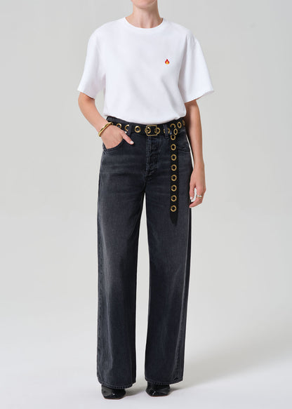 Person wearing a white t-shirt and dark jeans with button details on a plain background