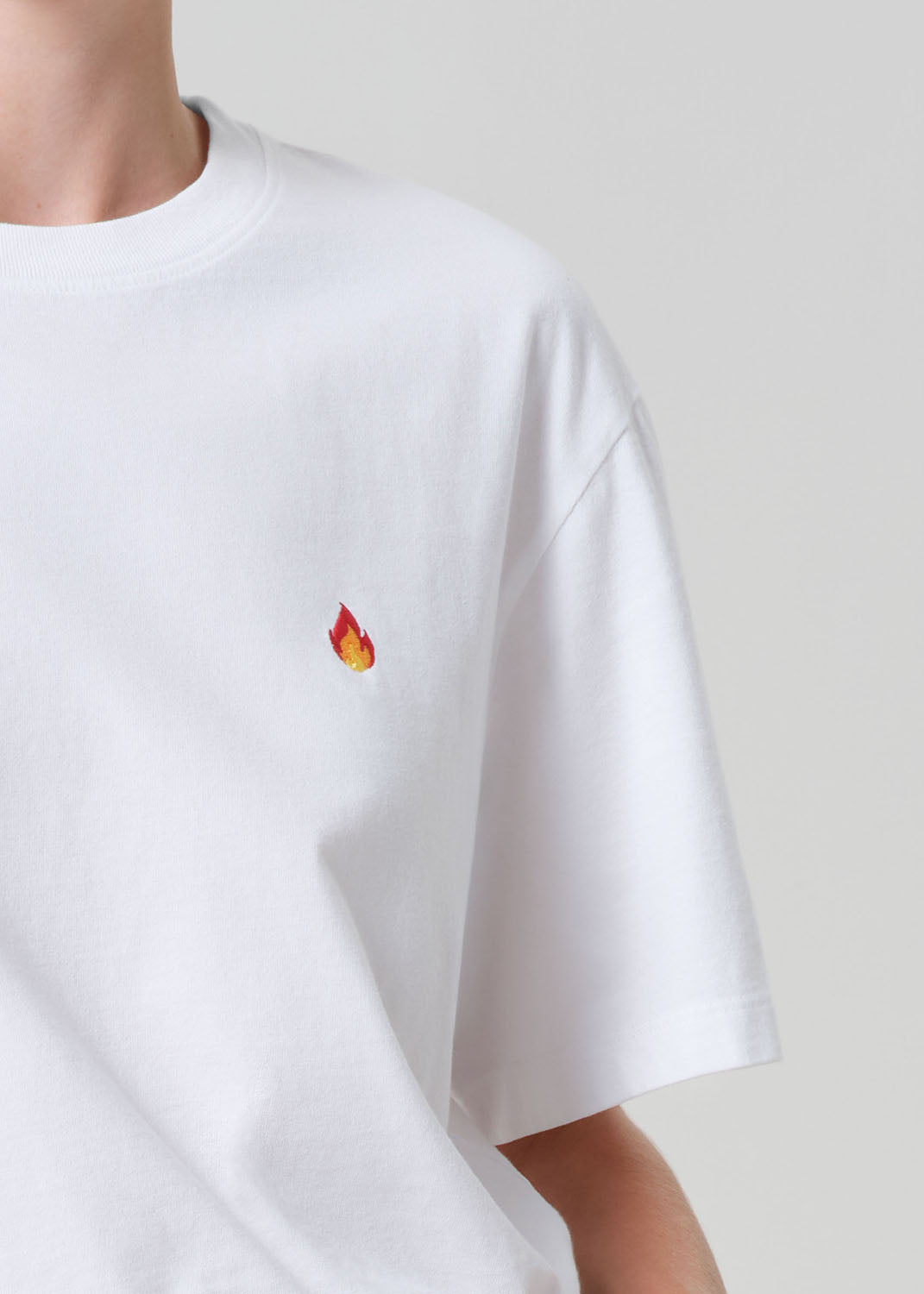 White t-shirt with a small red and yellow flame logo on a plain background