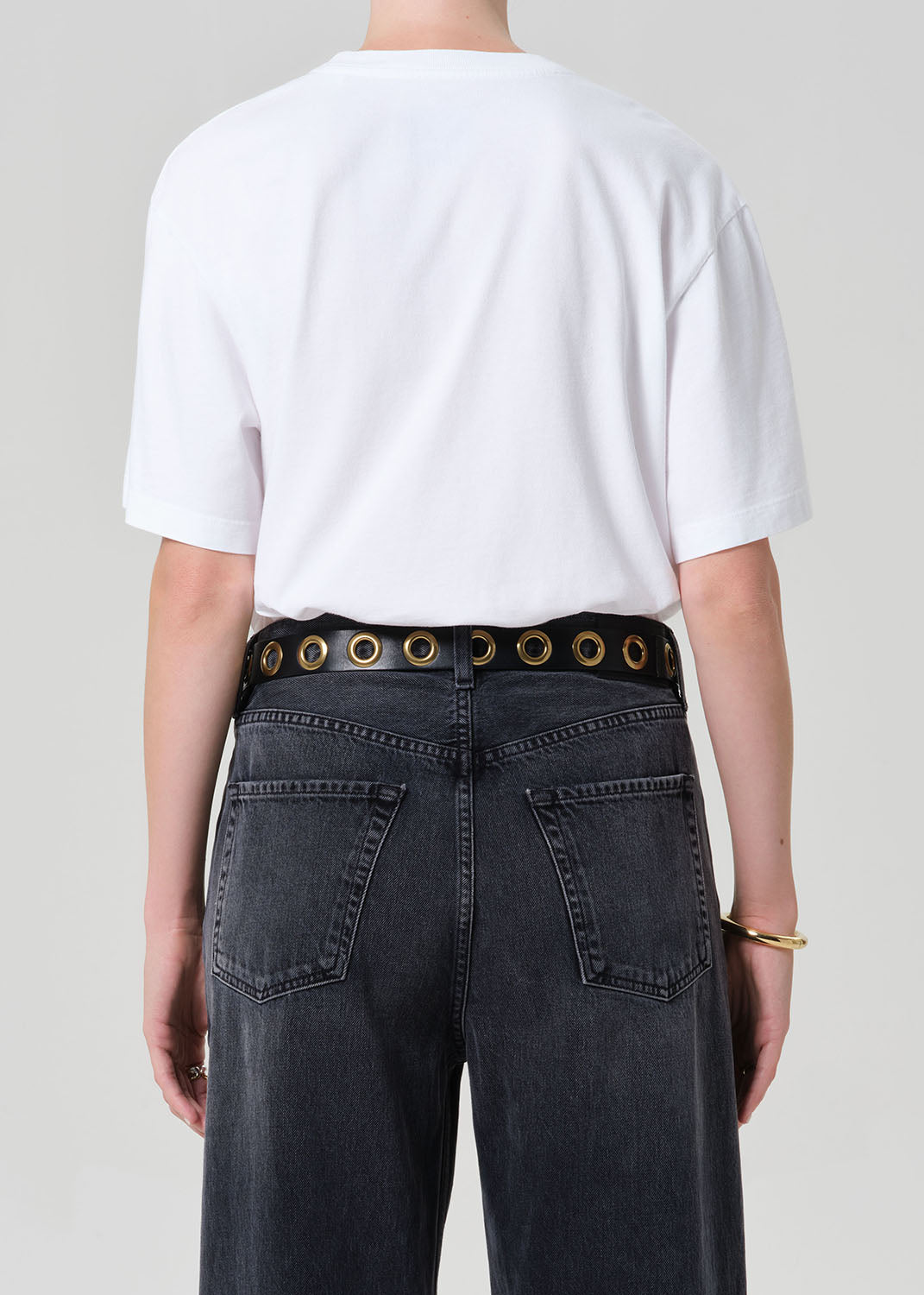 Person wearing a white t-shirt and black jeans with a belt on a plain background