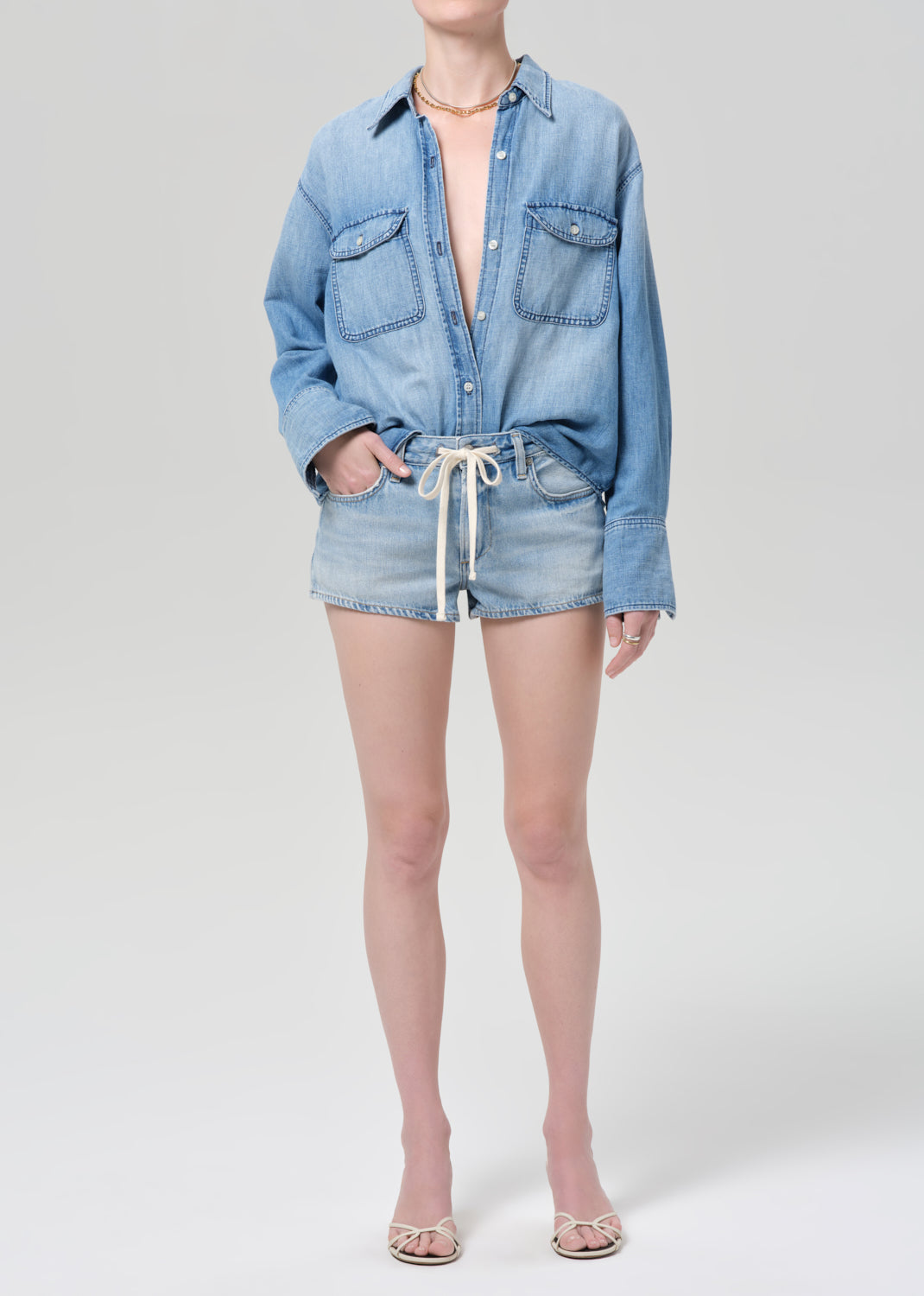 Person wearing a blue denim shirt and shorts on a plain background