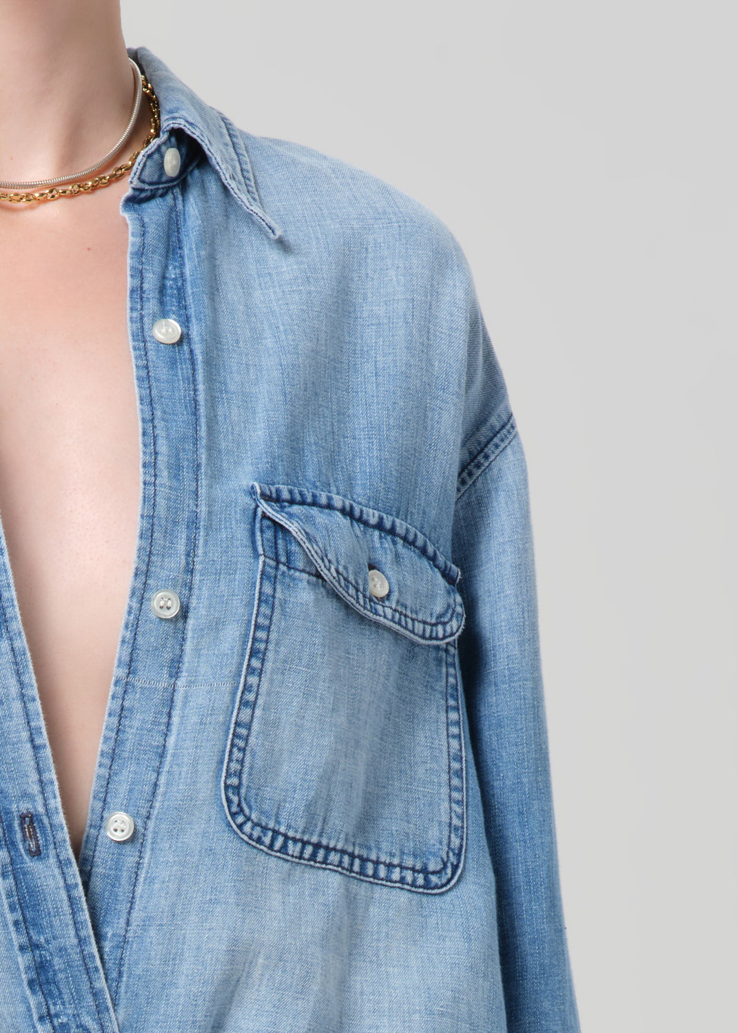 Person wearing a blue denim shirt and shorts on a plain background
