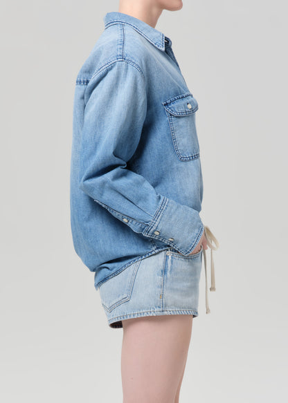 Person wearing a blue denim shirt and shorts on a plain background