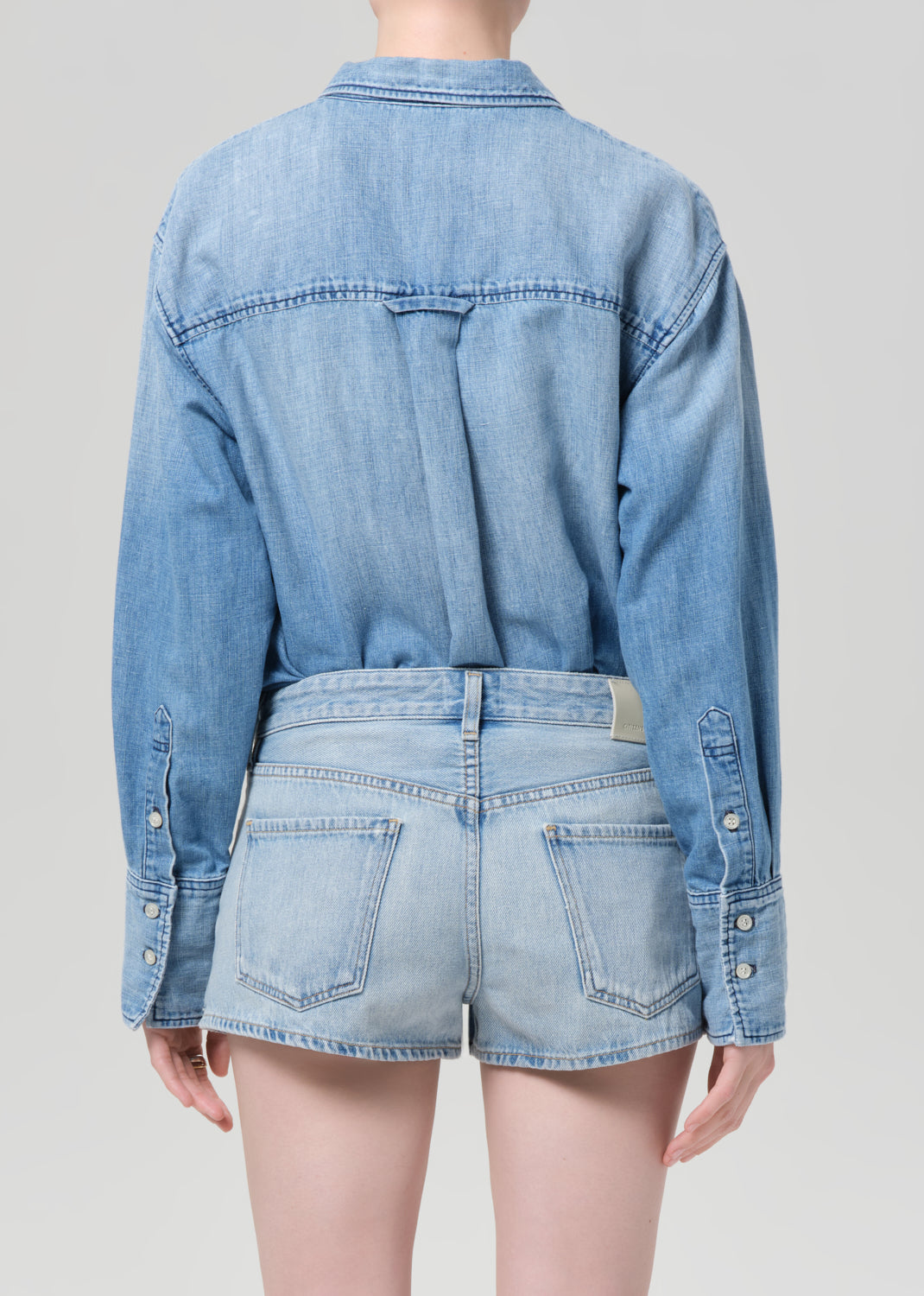 Person wearing a blue denim shirt and shorts on a plain background