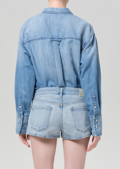 Person wearing a blue denim shirt and shorts on a plain background