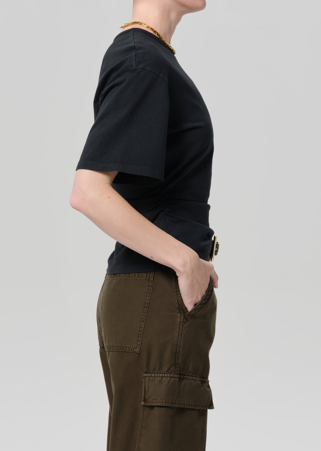 Person wearing a black t-shirt and brown cargo pants on a light gray background