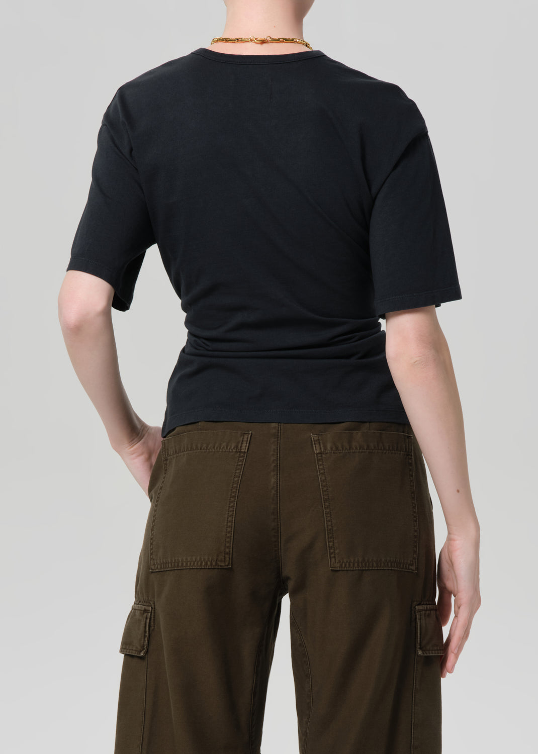 Person wearing a black t-shirt and brown cargo pants on a plain background