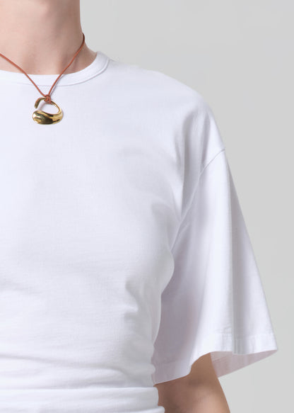 Person wearing a white t-shirt and a necklace with a gold pendant on a plain background